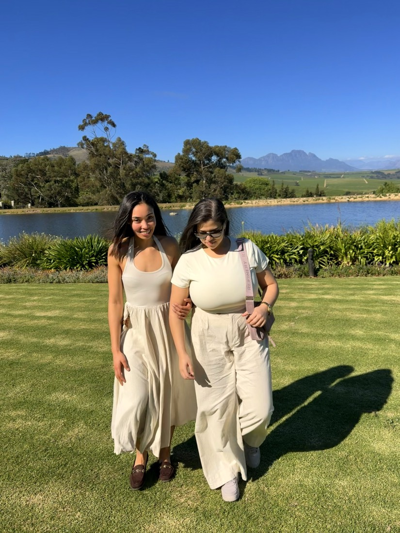 Two people walking arm in arm on a lawn by a lake with mountains behind